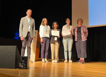 Five people standing on a stage with two holding certificates